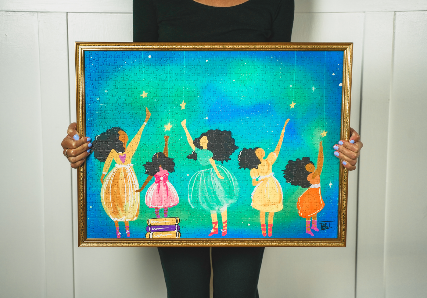 Woman holding a framed completed puzzle depicting girls reaching for stars
