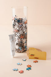 Glass jar filled with pieces from Mesa Sunrise accompanied by puzzle glue and straight edge tool