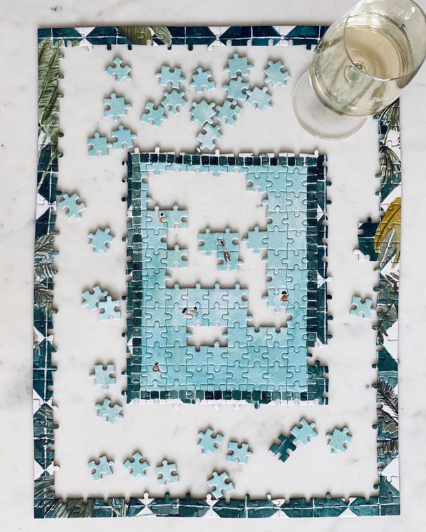 Half-completed Swim Club puzzle on marble table with glass of wine. 